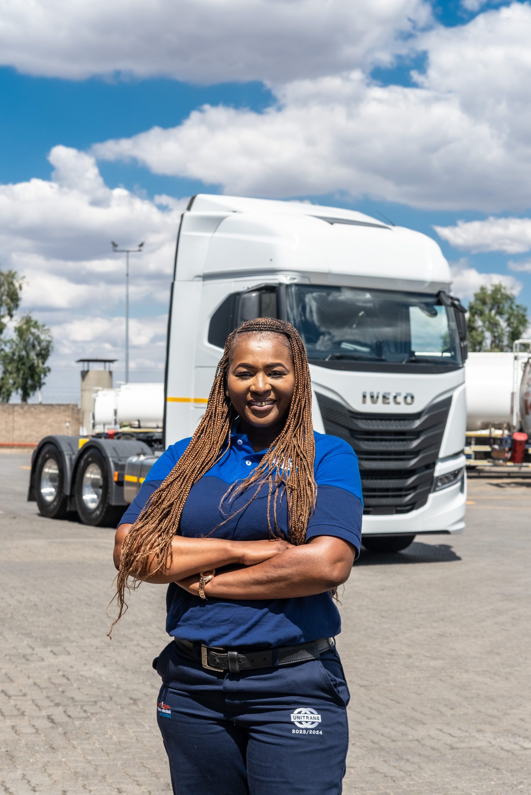 Female truck driver stands in front of parked truck with arms crossed